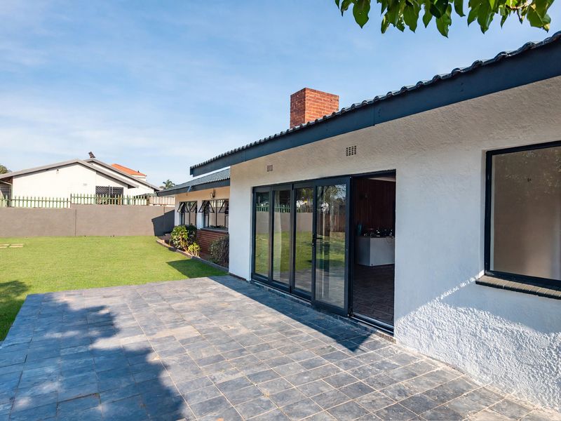A well-maintained rear exterior view featuring a paved patio area, sliding glass doors leading into the home, and a spacious lawn.