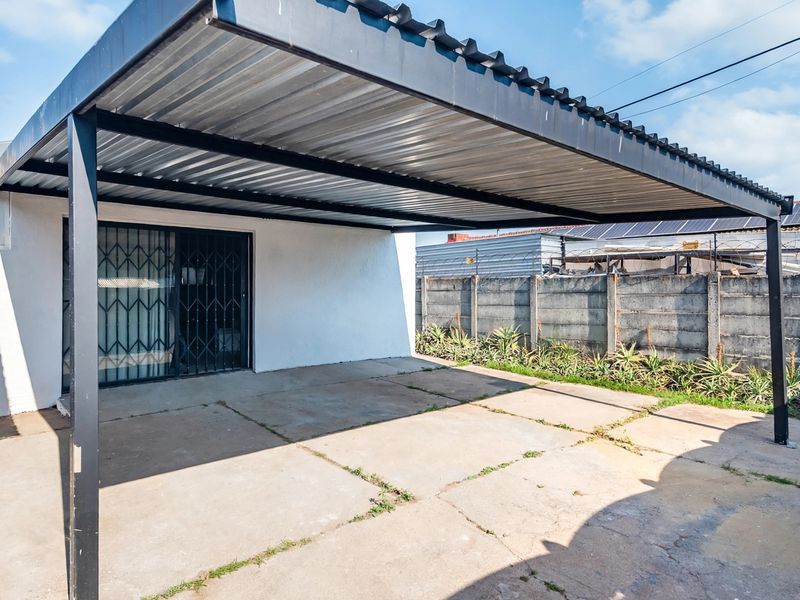 A covered outdoor patio area featuring a corrugated metal roof, steel support structure, and concrete flooring, providing a functional space for outdoor use.