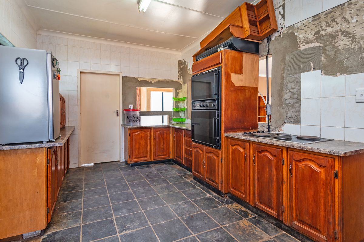 A kitchen featuring wooden cabinetry, a built-in double oven, and an electric hob, currently requiring significant wall repairs and cosmetic updates.