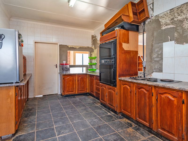 A kitchen featuring wooden cabinetry, a built-in double oven, and an electric hob, currently requiring significant wall repairs and cosmetic updates.