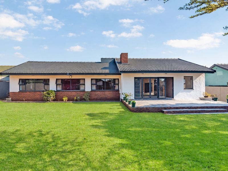 Rear view of a well-maintained house featuring a tiled roof, brick and stucco exterior, paved patio area, and a spacious lawn.