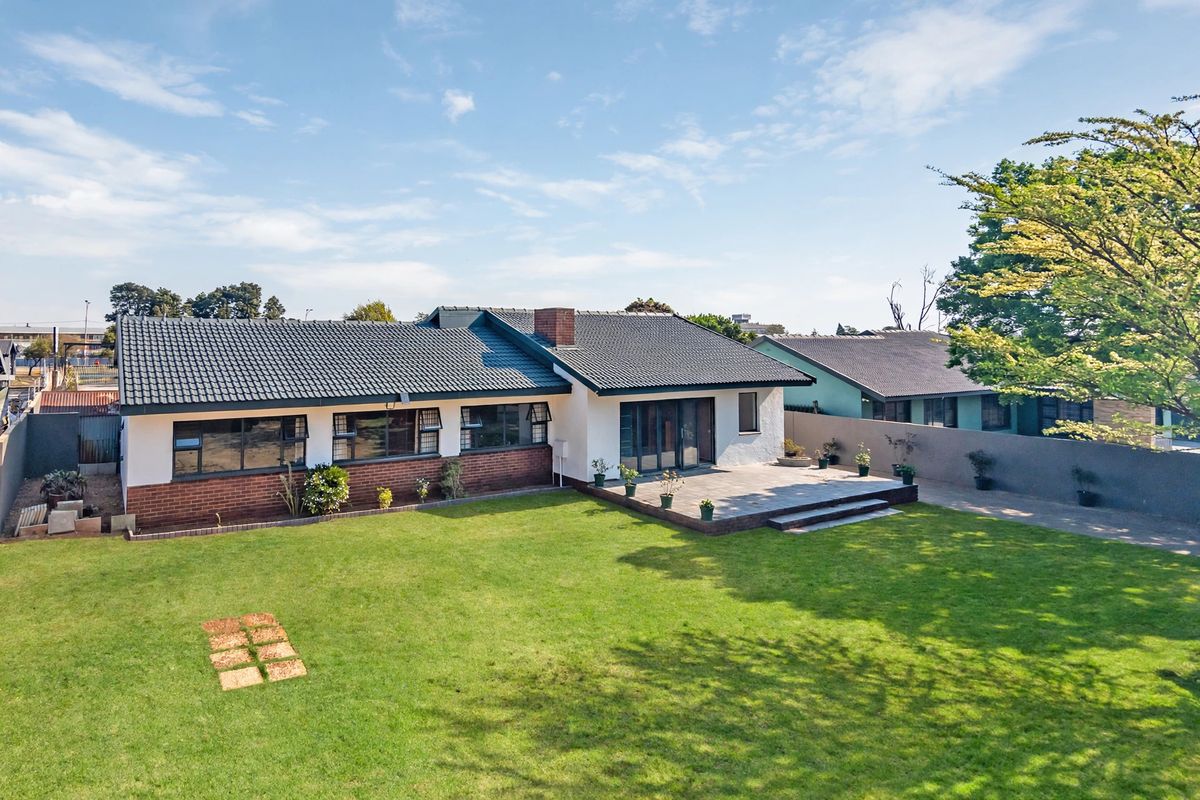 Rear view of a single-story residential home featuring a tiled roof, brick and rendered facade, and a paved patio area overlooking a spacious lawn.