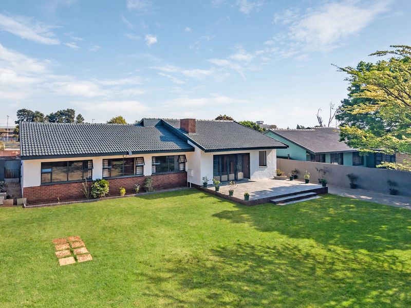 Rear view of a single-story residential home featuring a tiled roof, brick and rendered facade, and a paved patio area overlooking a spacious lawn.