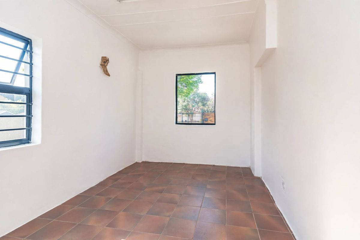 A bright, empty bedroom featuring tiled flooring, white walls, and windows fitted with security bars.