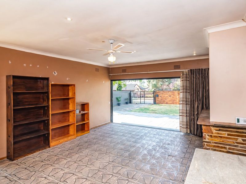 Spacious living area featuring tiled flooring, a ceiling fan, and large sliding doors opening to the rear garden, with a stone feature wall.