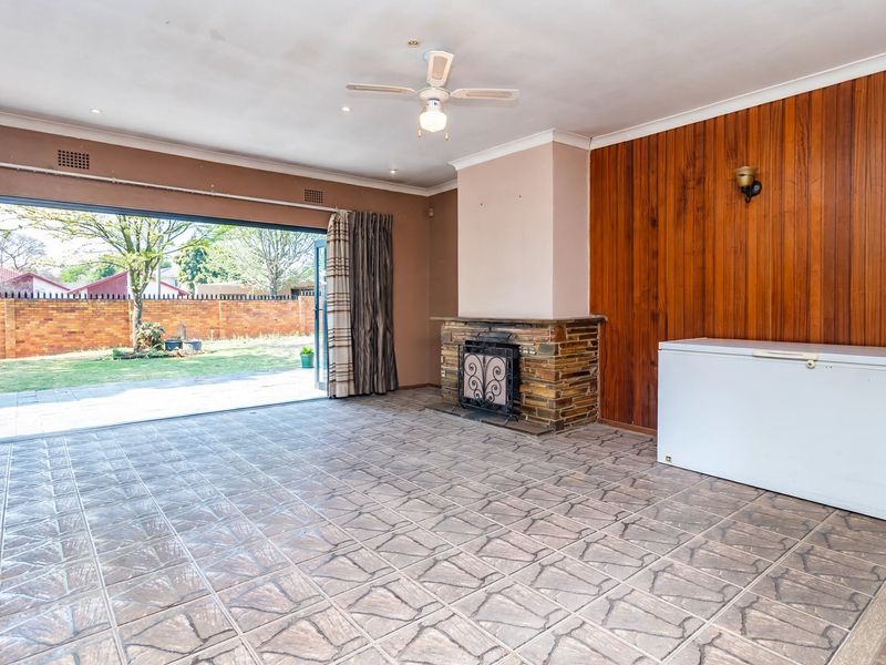 Spacious living room featuring a stone fireplace, wood paneling, tiled floors, and large sliding doors opening to the rear garden.