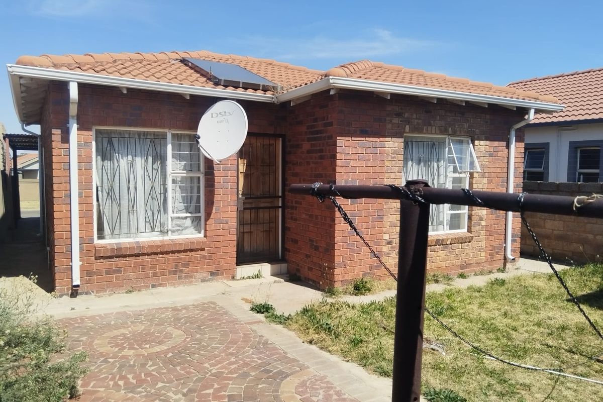 Rear view of a face brick house featuring a tiled roof, solar water heater, paved patio area, and security features on windows and doors.
