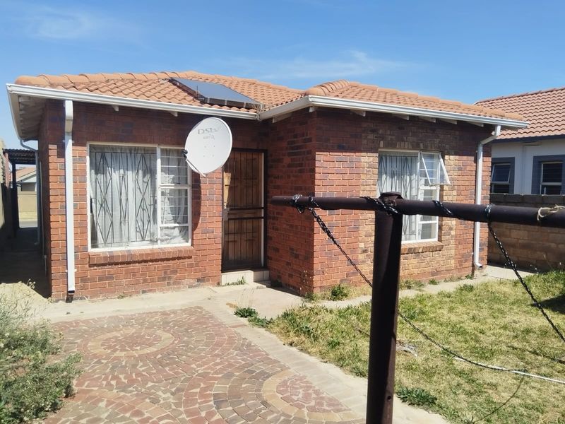 Rear view of a face brick house featuring a tiled roof, solar water heater, paved patio area, and security features on windows and doors.