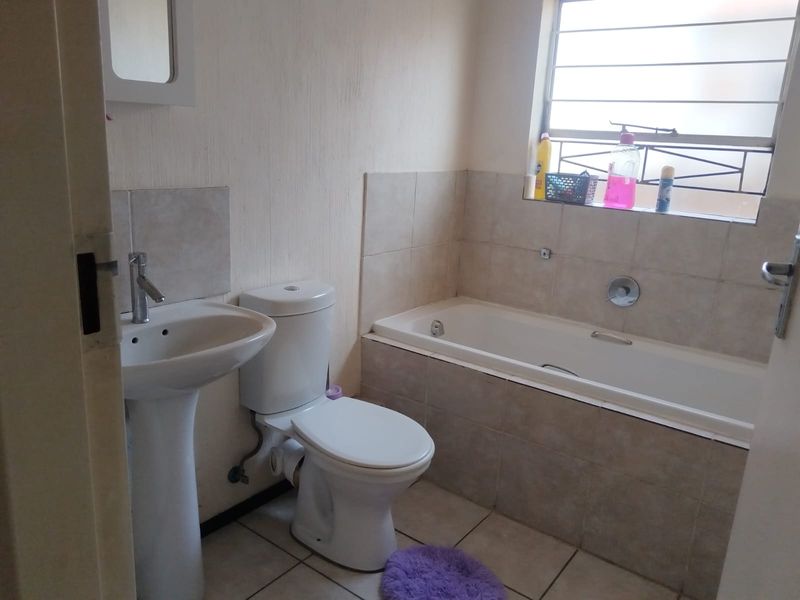 A functional bathroom featuring a pedestal basin, toilet, and a tiled built-in bathtub with security bars on the window.