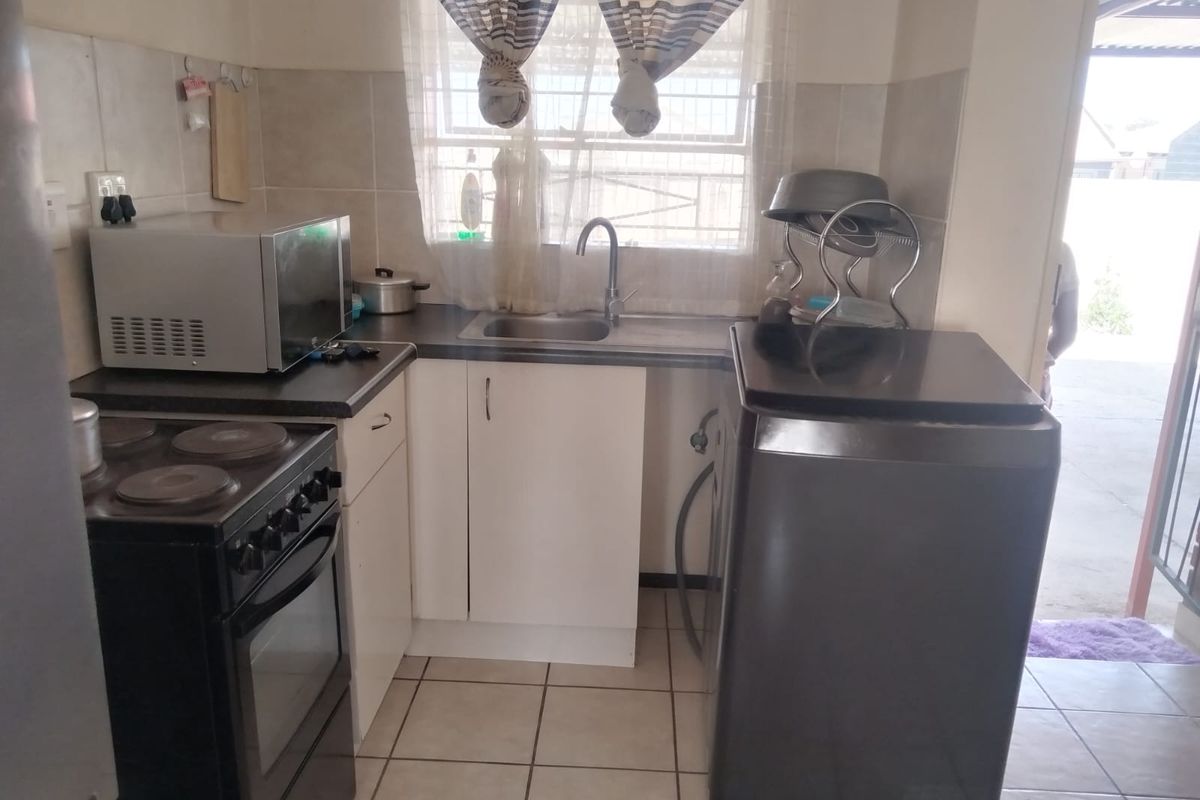 A compact kitchen featuring tiled flooring, a stainless steel sink, built-in cabinetry, and a tiled backsplash, providing a functional workspace.