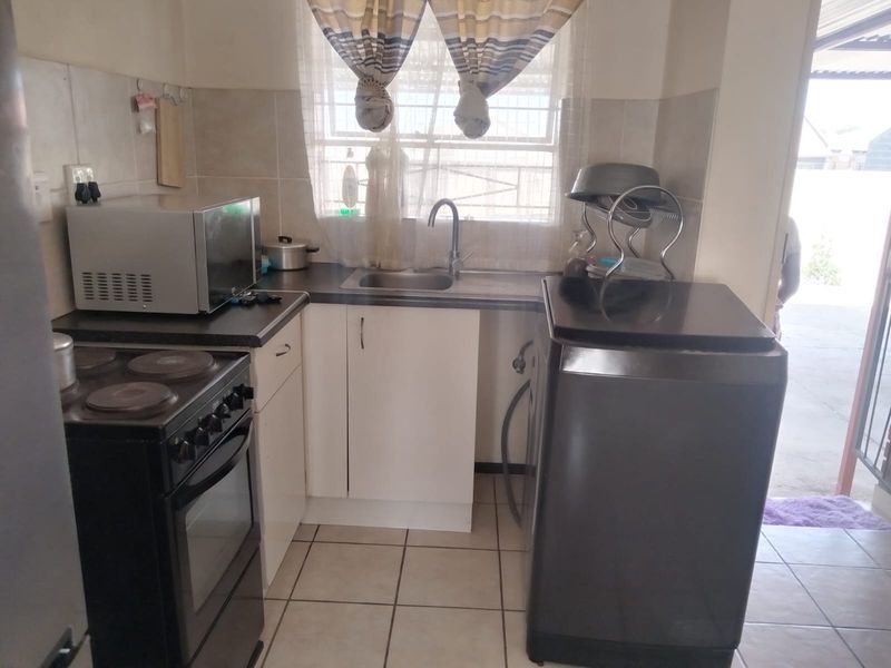 A compact kitchen featuring tiled flooring, a stainless steel sink, built-in cabinetry, and a tiled backsplash, providing a functional workspace.