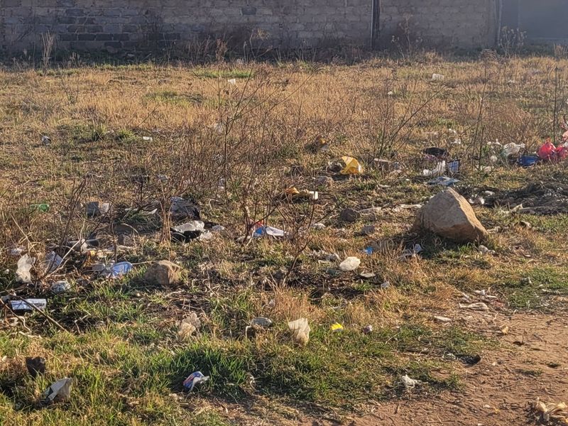 A vacant residential plot featuring dry grass, scattered debris, and a perimeter boundary wall.