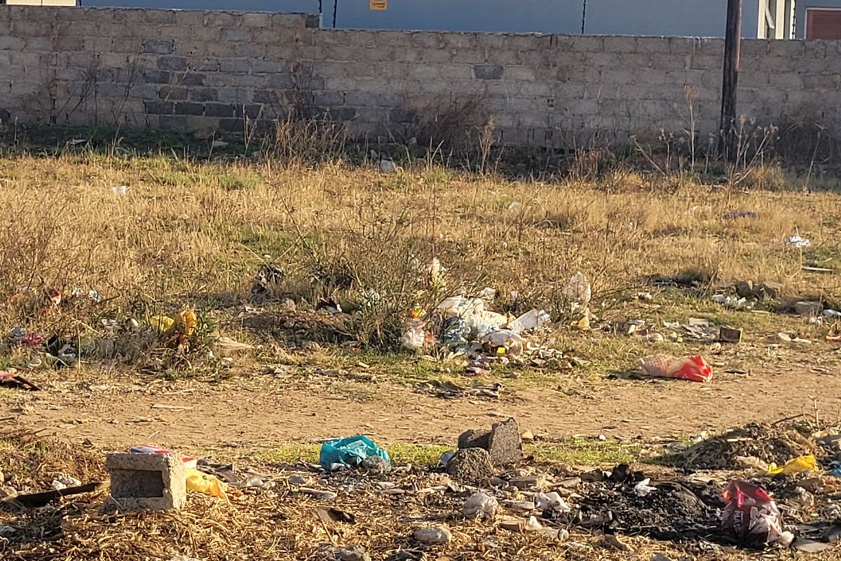 A vacant residential plot featuring a perimeter masonry wall with electric fencing, currently requiring significant site clearing and debris removal.
