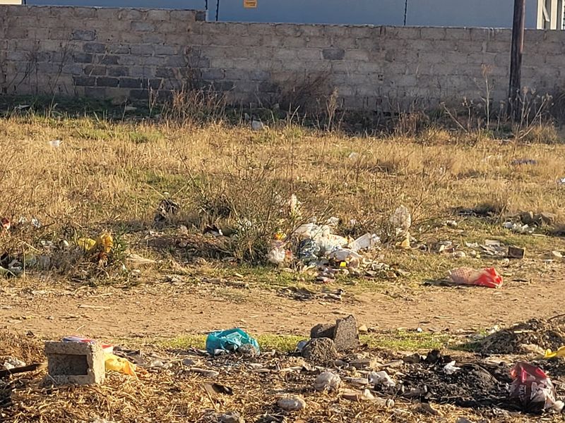 A vacant residential plot featuring a perimeter masonry wall with electric fencing, currently requiring significant site clearing and debris removal.