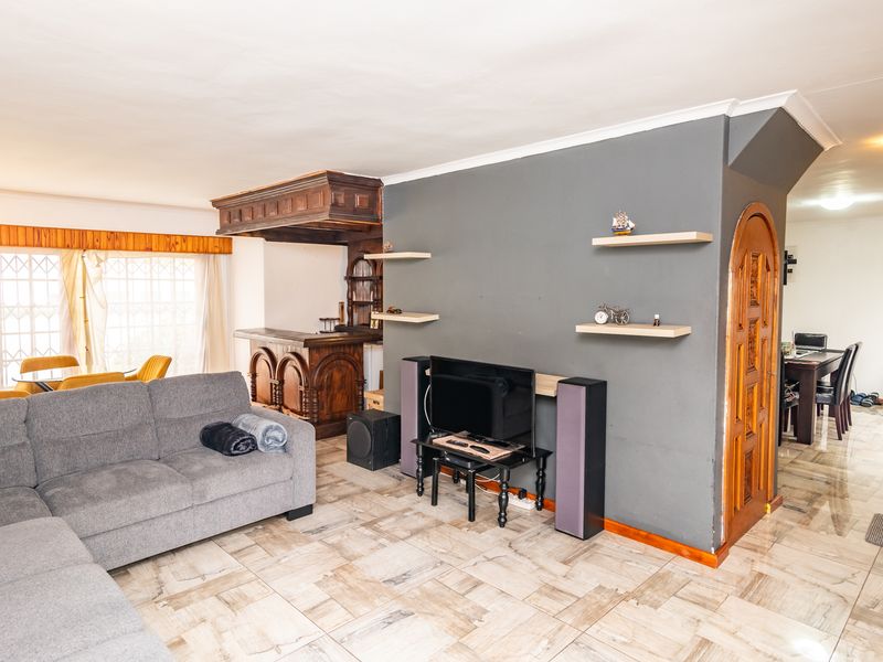 Open plan living area featuring a built-in wooden bar, tiled flooring, and an arched doorway leading to the dining space.