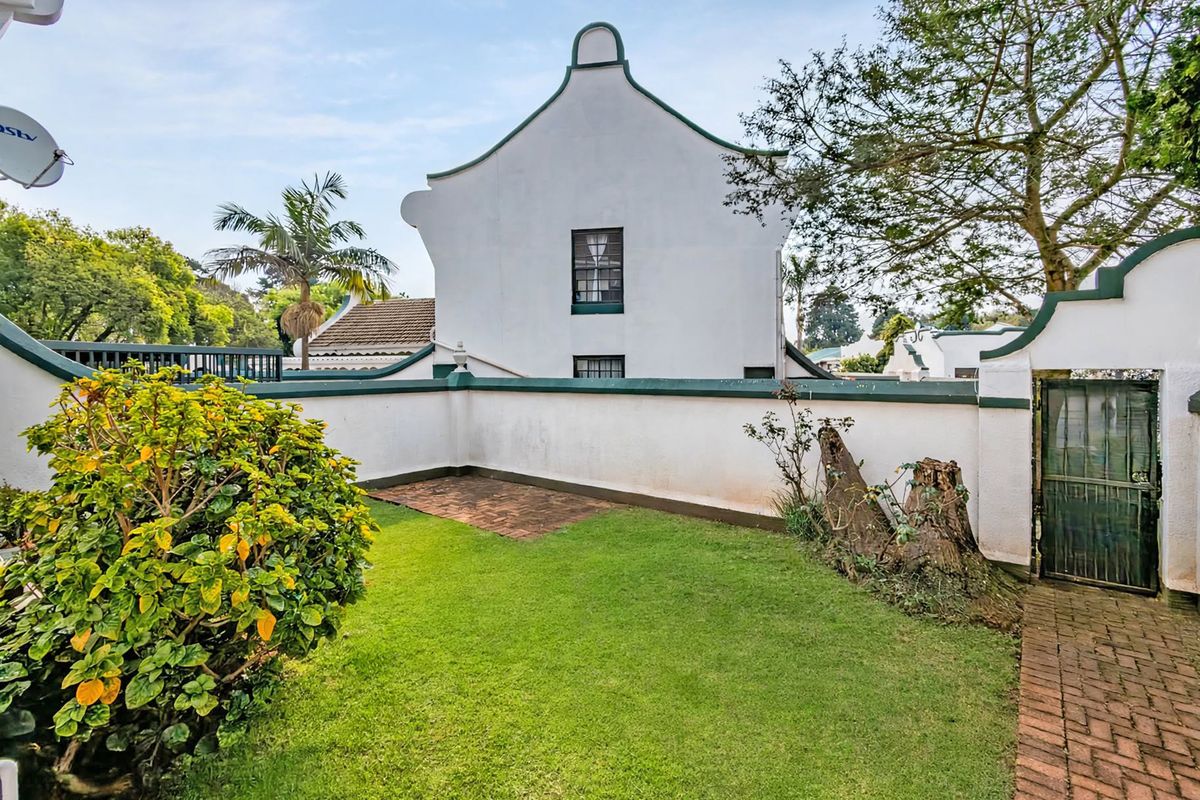 A private rear garden area featuring a lawn, brick paved section, and secure gated access, set against the backdrop of a traditional townhouse facade.