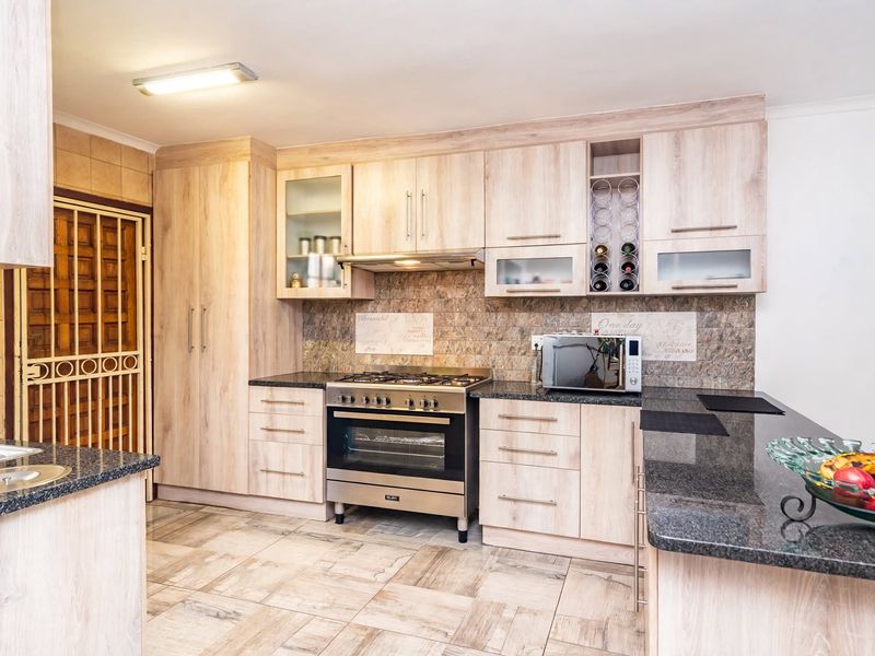 Modern kitchen featuring light wood cabinetry, granite countertops, a gas stove with extractor fan, and tiled flooring with an adjacent security gate.