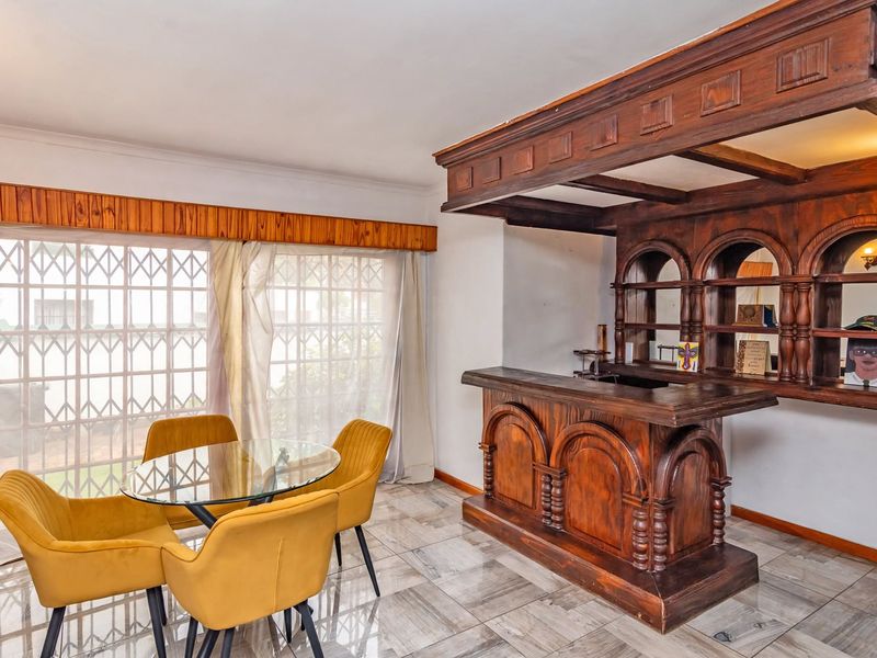 A dedicated bar area featuring a substantial built-in wooden bar counter and matching overhead shelving unit, complemented by tiled flooring and large windows.