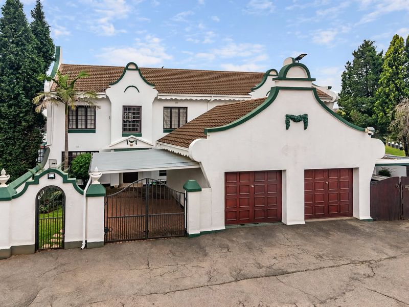 Front elevation of a townhouse featuring a double garage, gated entrance, carport, and traditional architectural detailing with a tiled roof.