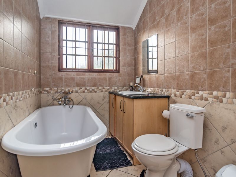 A functional bathroom featuring a freestanding bathtub, vanity cabinet with basin, and toilet, finished with neutral wall and floor tiling.