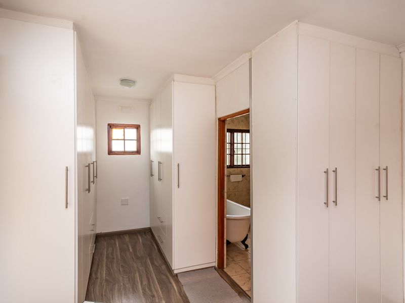 A bright hallway featuring extensive built-in white cabinetry, laminate flooring, and direct access to an adjoining bathroom.