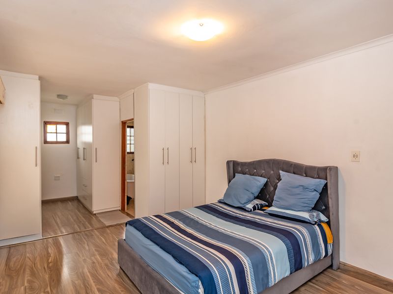 A well-maintained bedroom featuring laminate flooring, extensive built-in cupboard storage, and direct access to an en-suite bathroom.