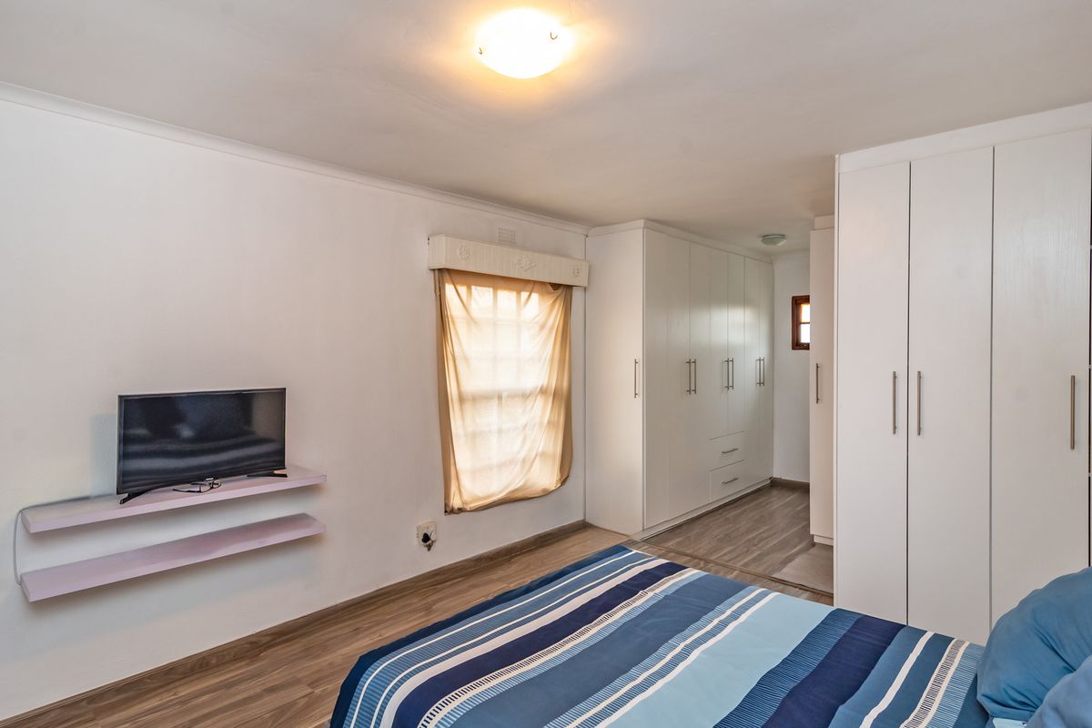 A well-maintained bedroom featuring extensive built-in cupboards, modern laminate flooring, and neutral wall finishes.