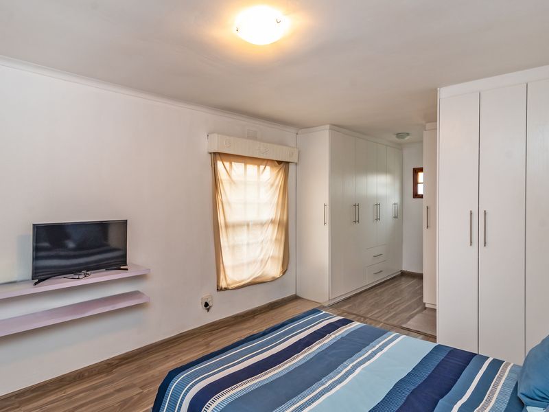 A well-maintained bedroom featuring extensive built-in cupboards, modern laminate flooring, and neutral wall finishes.