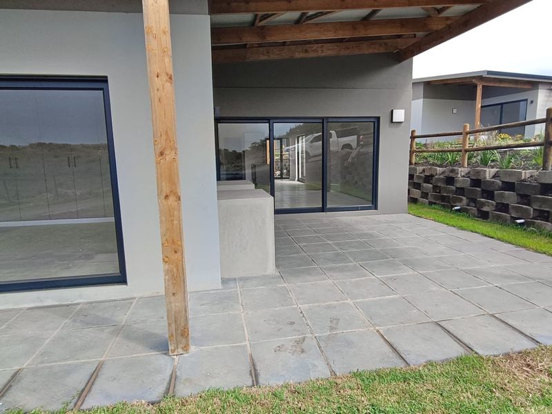 A covered outdoor patio area featuring paved flooring, a timber support post, and sliding glass doors leading into the interior living space.