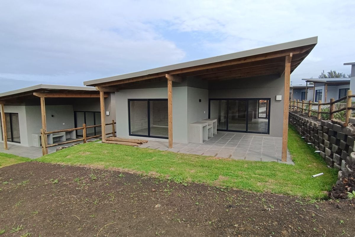Rear view of a modern cluster home featuring a covered patio with a built-in braai, sliding glass doors, and an adjacent landscaped garden area.