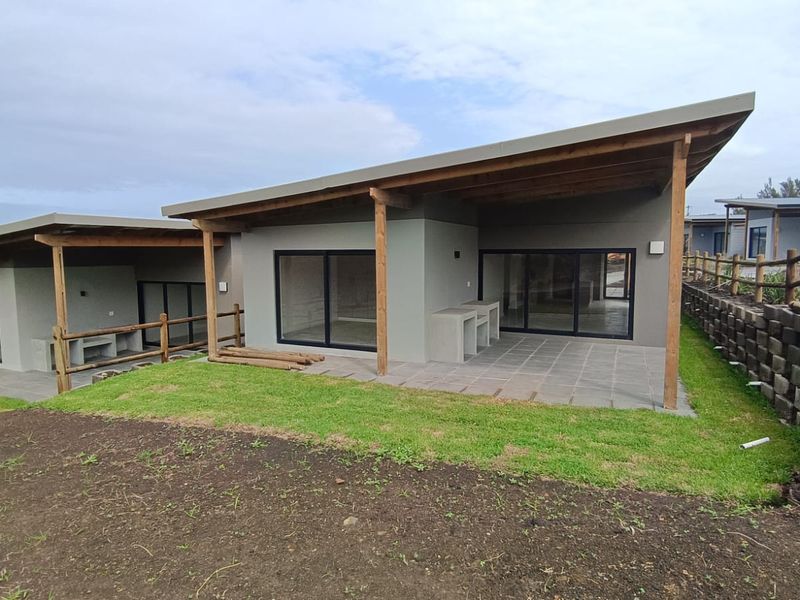 Rear view of a modern cluster home featuring a covered patio with a built-in braai, sliding glass doors, and an adjacent landscaped garden area.
