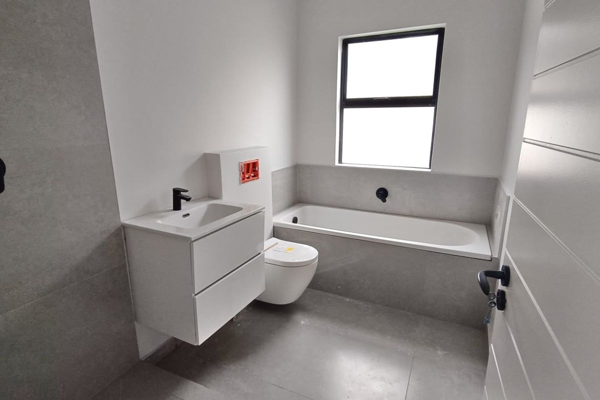 Modern bathroom featuring a wall-hung vanity, wall-hung toilet, and built-in bathtub with contemporary black matte fixtures and neutral grey tiling.