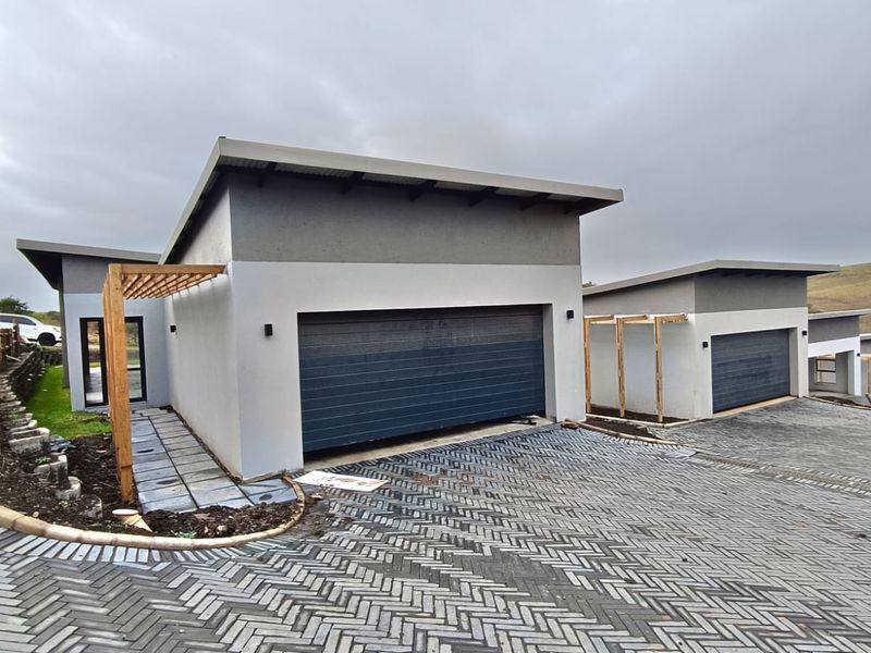 Modern cluster home exterior featuring a paved driveway, garage access, and timber pergola structures in a developing estate setting.