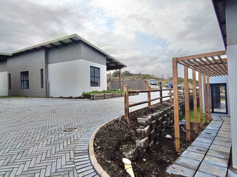 Front exterior view of a modern cluster home featuring a herringbone paved driveway, timber pergola, and tiered retaining walls with ongoing landscaping.