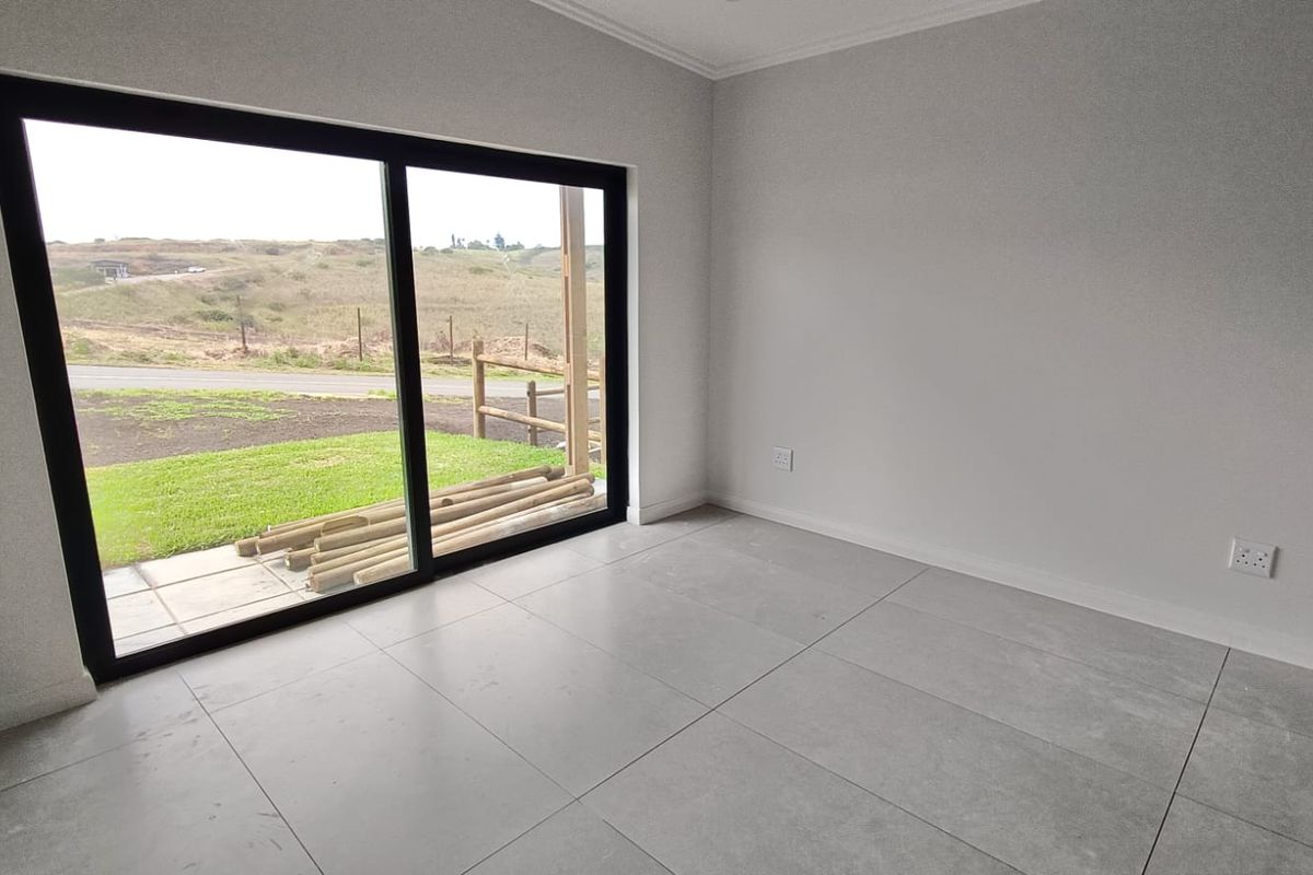 A bright, empty bedroom featuring large sliding glass doors that open to an outdoor area, finished with modern grey floor tiles.
