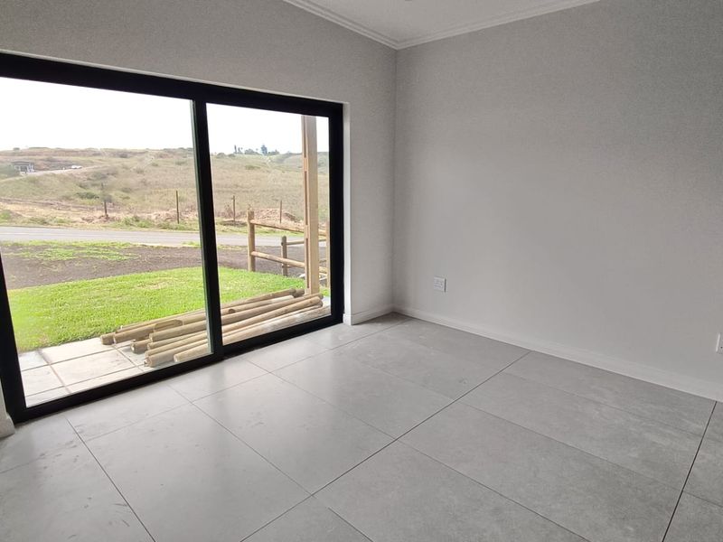 A bright, empty bedroom featuring large sliding glass doors that open to an outdoor area, finished with modern grey floor tiles.