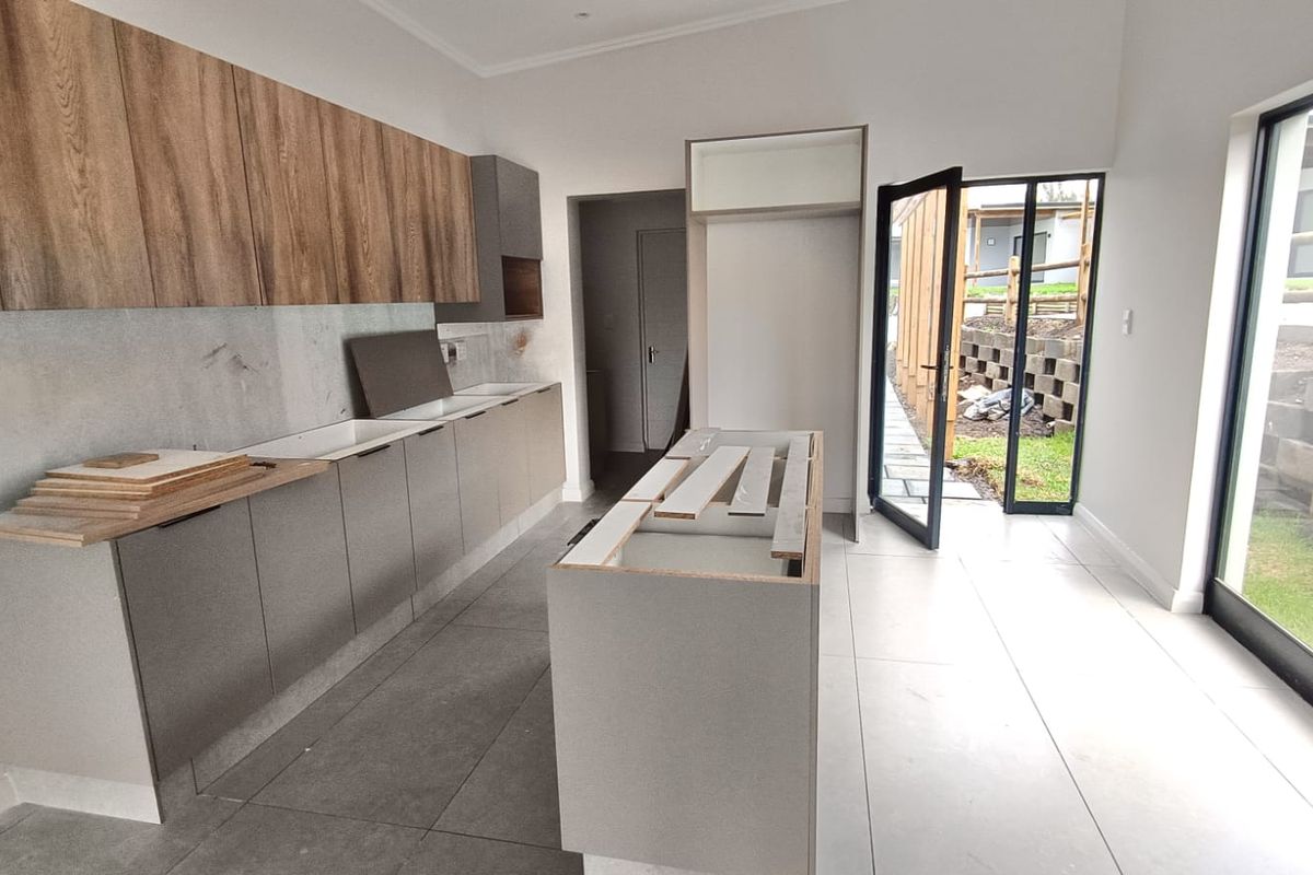 A modern, unfinished kitchen featuring contemporary grey and wood-tone cabinetry, a central island, and large sliding doors leading to an outdoor area.