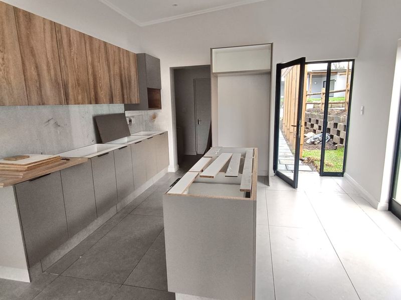 A modern, unfinished kitchen featuring contemporary grey and wood-tone cabinetry, a central island, and large sliding doors leading to an outdoor area.