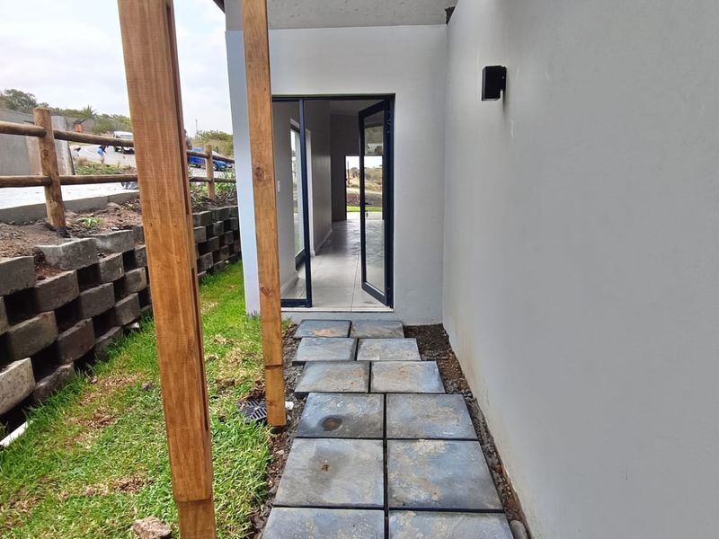 A side pathway featuring stone pavers leading to an aluminium glass door, flanked by a retaining wall and timber structural posts.