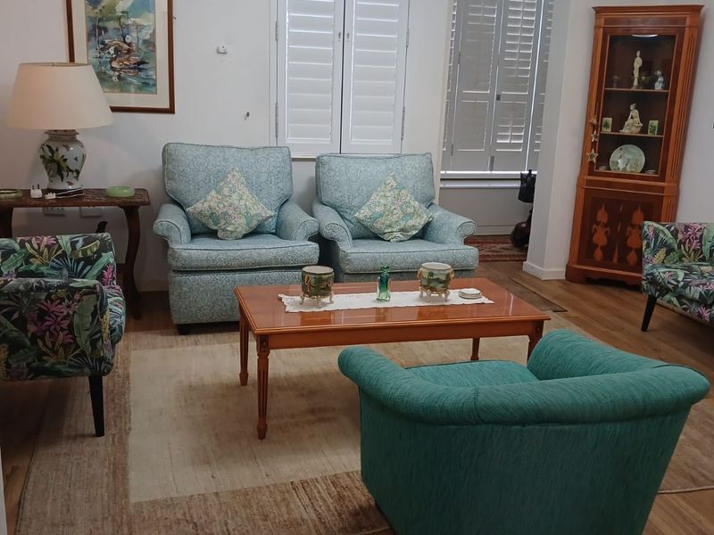 A comfortable living room featuring laminate flooring, plantation shutters, and a wall-mounted air conditioning unit.