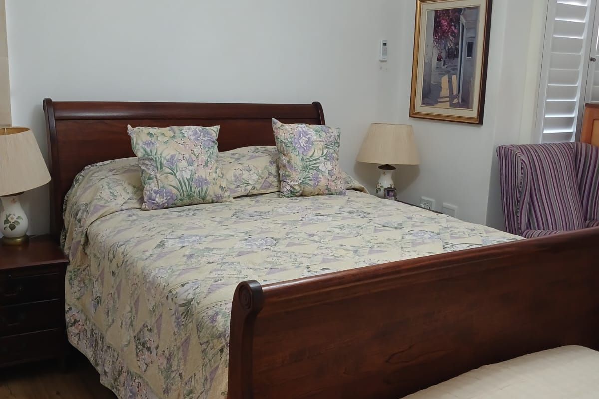 A well-maintained bedroom featuring laminate flooring, plantation shutters, and a wall-mounted split-system air conditioner for climate control.