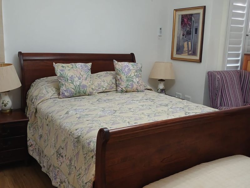 A well-maintained bedroom featuring laminate flooring, plantation shutters, and a wall-mounted split-system air conditioner for climate control.
