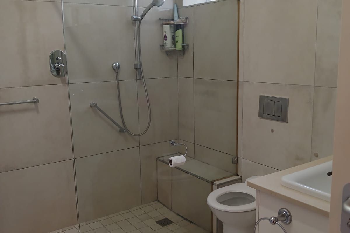 Modern bathroom featuring a walk-in shower with glass screen, wall-hung toilet with concealed cistern, and a vanity basin with neutral floor-to-ceiling tiling.