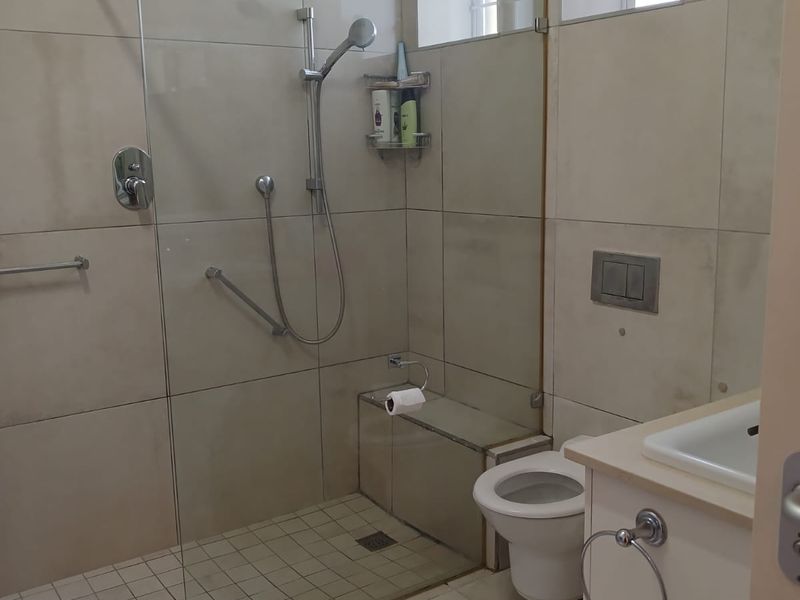 Modern bathroom featuring a walk-in shower with glass screen, wall-hung toilet with concealed cistern, and a vanity basin with neutral floor-to-ceiling tiling.