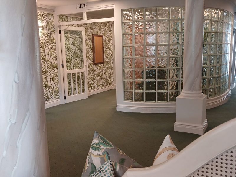 A well-lit retirement village hallway featuring decorative columns, a curved glass block wall, and dedicated lift access.