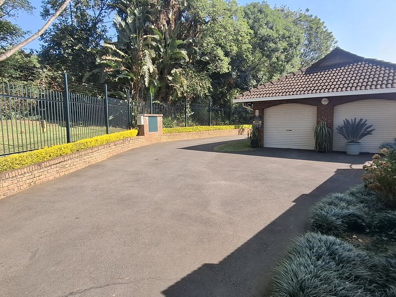 Front exterior view of the townhouse featuring a double garage, paved driveway, and secure perimeter walling with steel fencing.