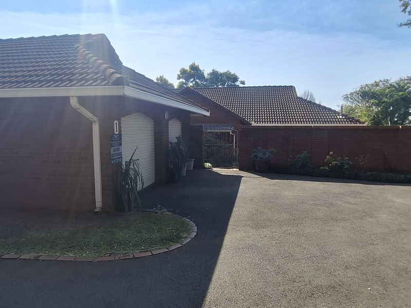 Front exterior view of a brick townhouse featuring a double garage, paved driveway, and secure perimeter fencing.