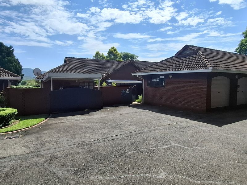 Front exterior view of the townhouse complex featuring brick facades, tiled roofs, a shared asphalt driveway, and integrated garage access.