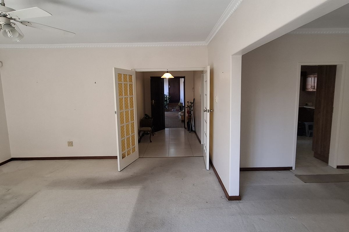 An empty living room featuring crown molding, a ceiling fan, and french doors leading to an adjacent hallway.