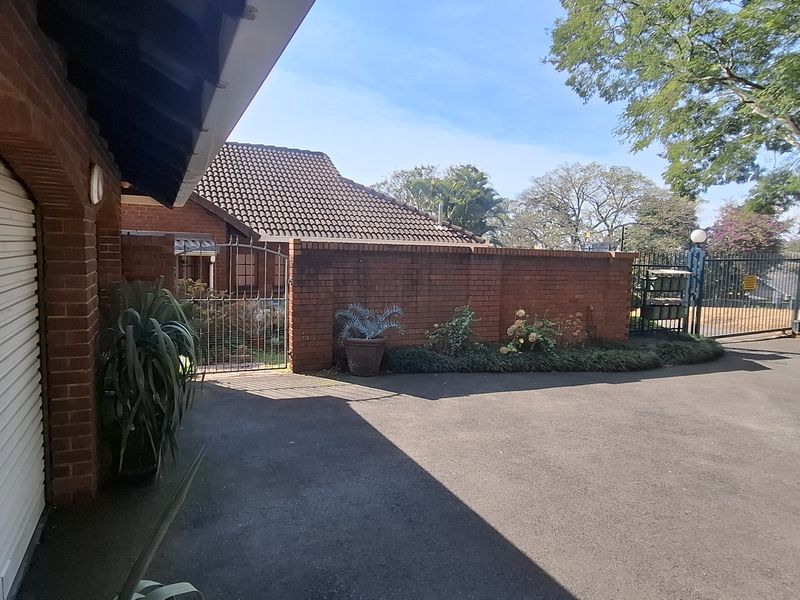 Front exterior view of the townhouse featuring a brick boundary wall, asphalt driveway, and secure gated entrance.